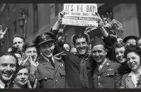 A crowd gathers in Times Square celebrating with a newspaper announcing the surrender of Germany. (Photo Credit: Corbis)